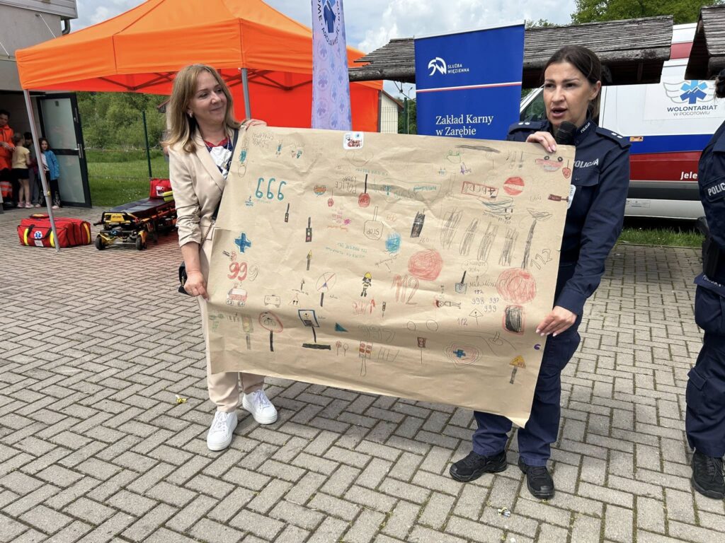 Leśna akcja "bezpieczna droga do szkoły" na zdjęciu rzecznik policji w Lubaniu przed stanowiskiem wolontariatu pogotowia ratunkowego